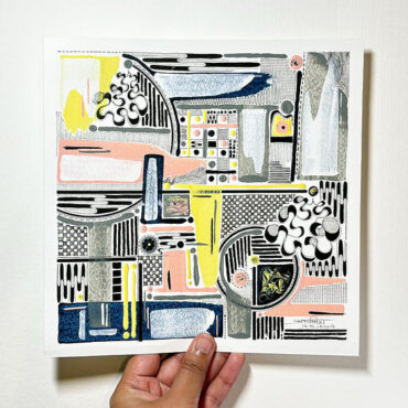 A hand holding a square piece of abstract art featuring a complex mix of geometric shapes, patterns, and colors including black, white, yellow, pink, and blue. The artwork includes intricate designs with various lines, circles, and textured areas, creating a visually engaging composition.